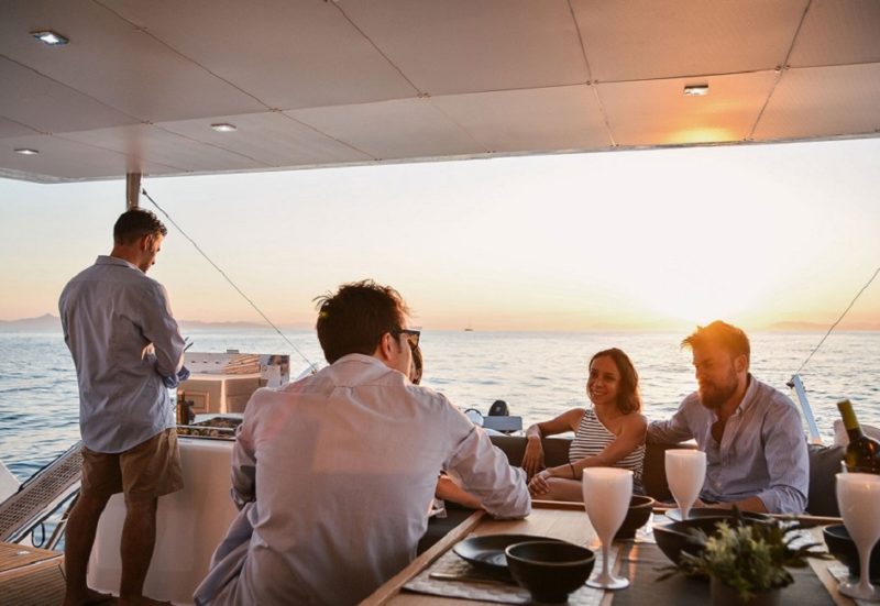 Repas entre amis sur le pont d'un catamaran moderne dans les Cyclades - Grèce | Au Tigre Vanillé